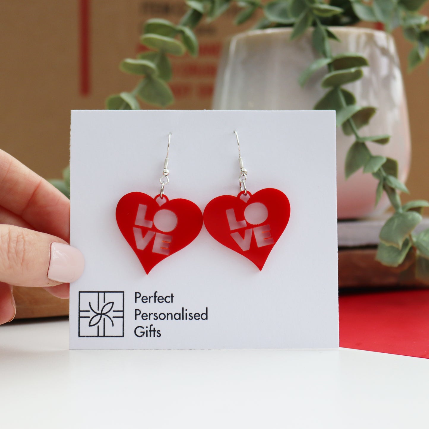 modern laser cut acrylic red valentines earrings with the word LOVE cut out from the centre of the heart shape on a plated silver hook